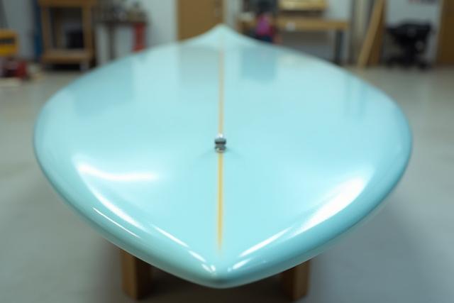 A newly shaped and glassed performance shortboard gleaming in the sunlight inside the studio.